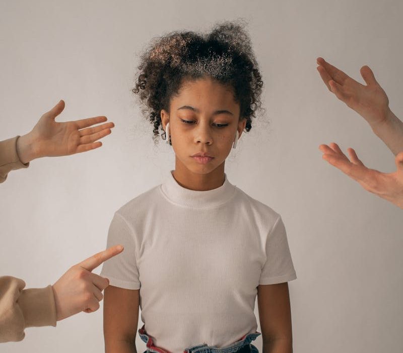 Crop people scolding disappointed African American teenage girl in casual wear standing on white background with sad face in studio